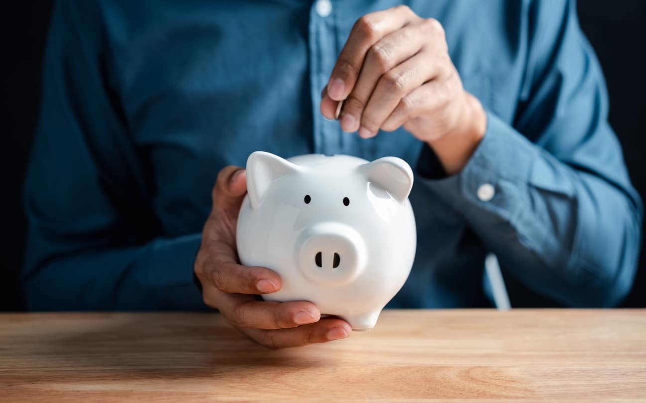 Person saving money in a white piggy bank, symbolising investment and financial growth.