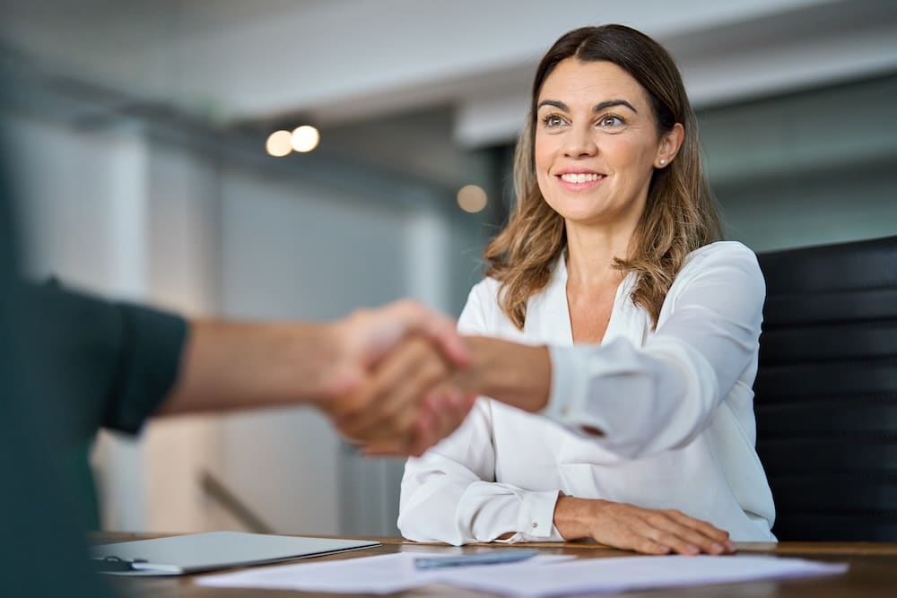 Female business broker smiling and shaking a client's hand